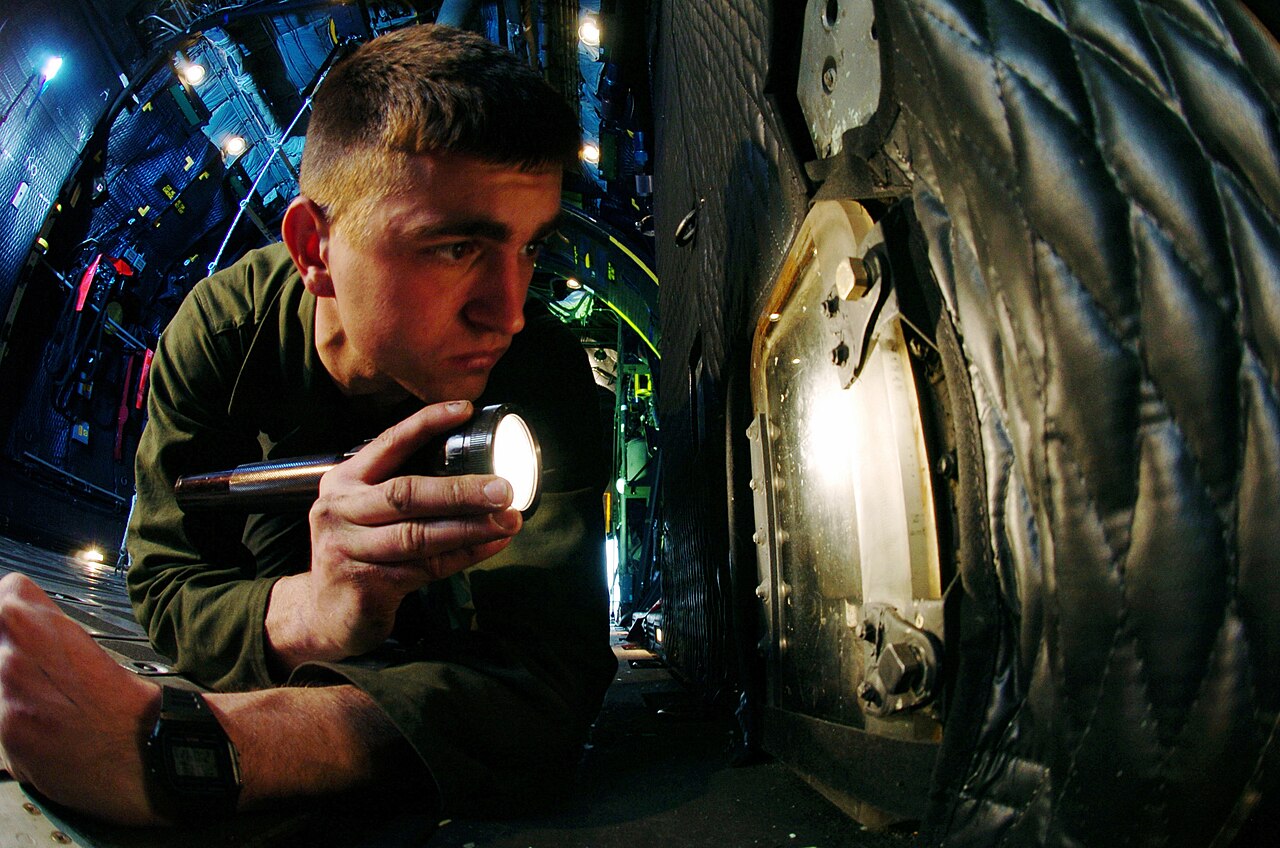 An Air Force crew chief uses a flashlight to check the main landing gear battery assembly of a C-130 Hercules during the airplane's annual inspection at Yokota Air Base, Japan, March 29, 2005. Photo: Master Sgt. Val Gempis, U.S. Air Force, public domain, via Wikimedia Commons.