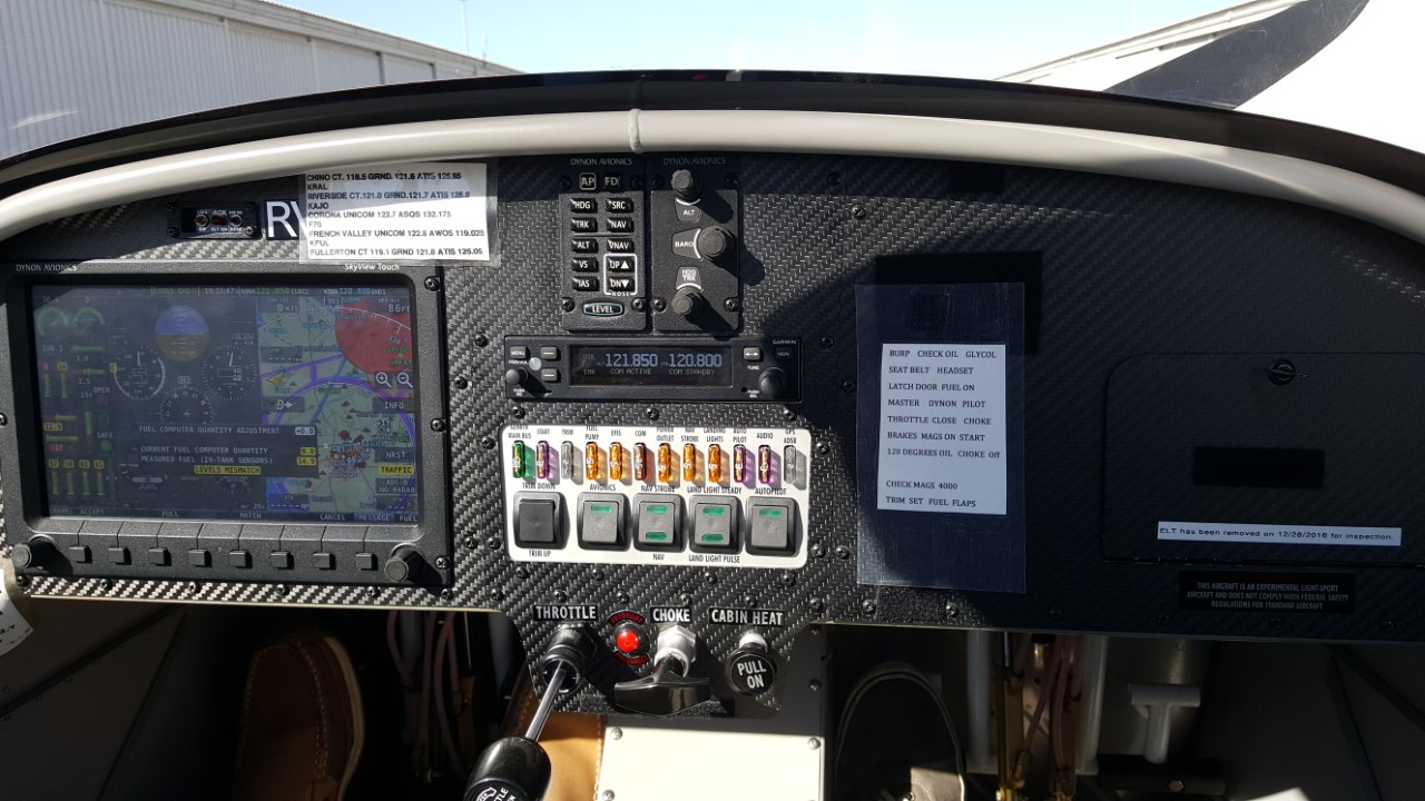 The instrument panel of a Van's RV-12 light-sport airplane: a Dynon SkyView Touch display, the Dynon autopilot and knob panels, a Garmin COM radio, a row of breakers and switches, and below them the wire bundles running down behind the throttle and choke. Photo: Don Ramey Logan, CC BY-SA 4.0, via Wikimedia Commons.